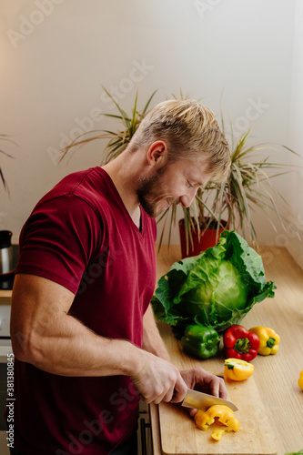 Happy handsome man is cooking in the kitchen by the window. Cut vegetables. Fresh bell peppers, cabbage and mint. Harvesting. selective focus