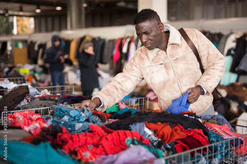 Obraz premium african american guy chooses sacond hands clothes at flea market