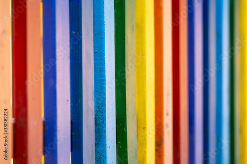 Part of wooden, rainbow colorful painted fence on a sunny hot summer day in a city park. Abstract multicolored background.