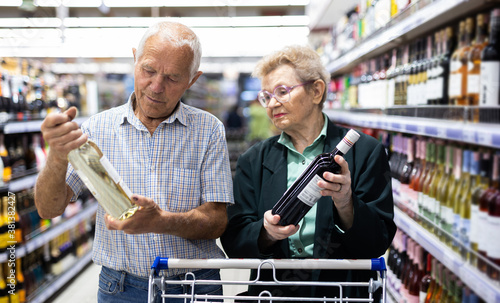 mature couple chooses bottle of wine in alcohol section of supermarket