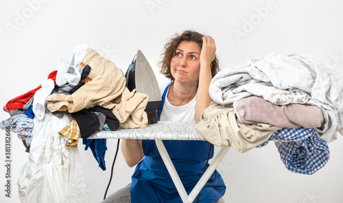 A woman holds an iron in her hands and sits at the ironing table. dirty laundry before ironing after washing. cleaning and washing and ironing concept