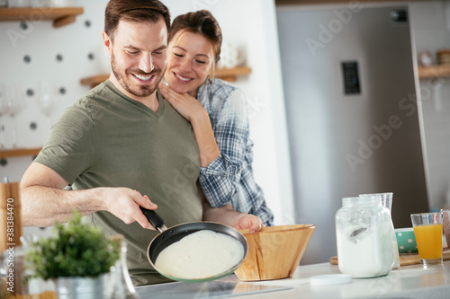 Young couple making pancakes at home. Loving couple having fun while cooking.