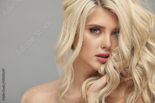Beauty portrait of caucasian woman with blonde curly hair on beige isolated
