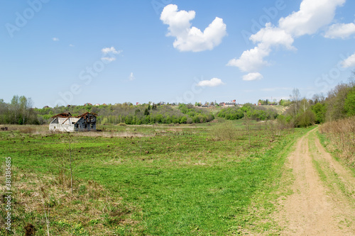 There is dry grass in the foreground. On the middle plan on the green field is an old  destroyed house. In the background is a hill with rural houses.