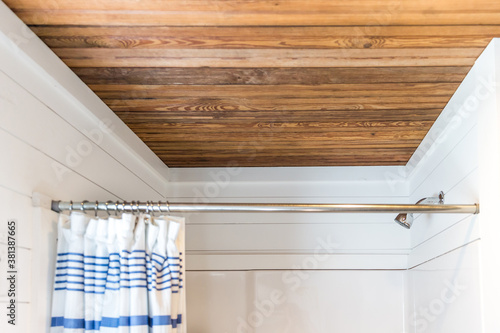 Small and compact bathroom shower stall in a small farmhouse decor inspired cabin with a blue striped shower curtain, hooks on the wall and a rustic wood plank ceiling