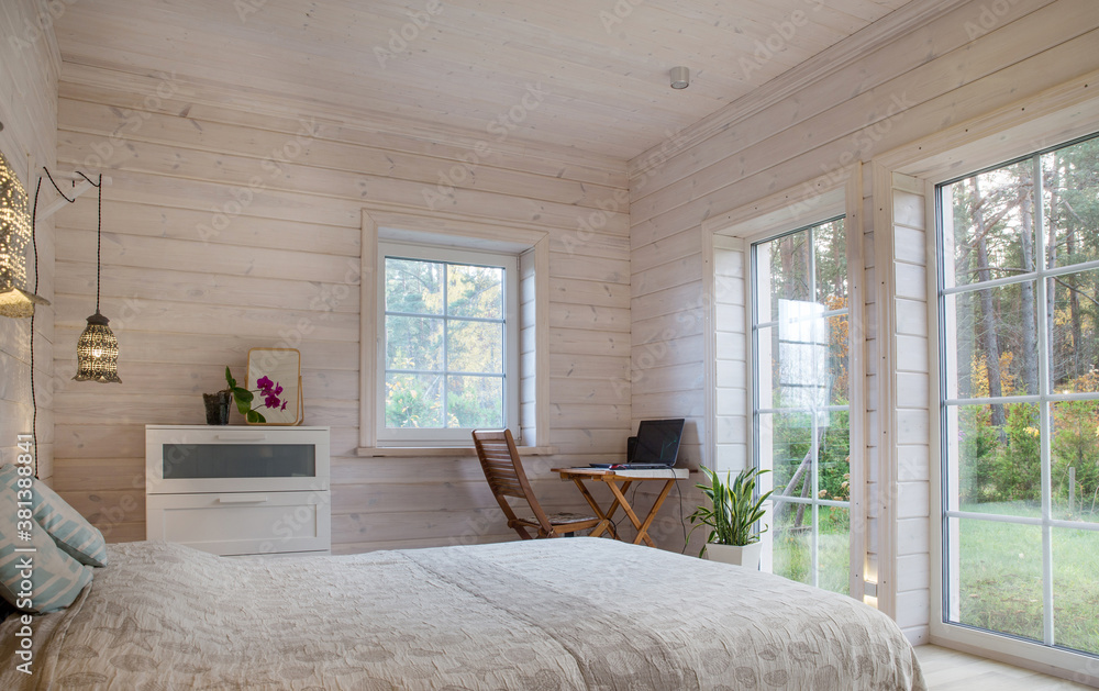 White bedroom with simple decor items in a stylish wooden house. Workplace in the bedroom, a table and a computer