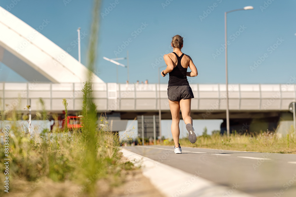 Back view of sportswoman jogging outdoors during a day.