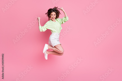 Full body profile photo of attractive crazy lady jump up celebrate great win raise fists wear casual green crop pullover naked belly jeans short skirt shoes isolated pink color background