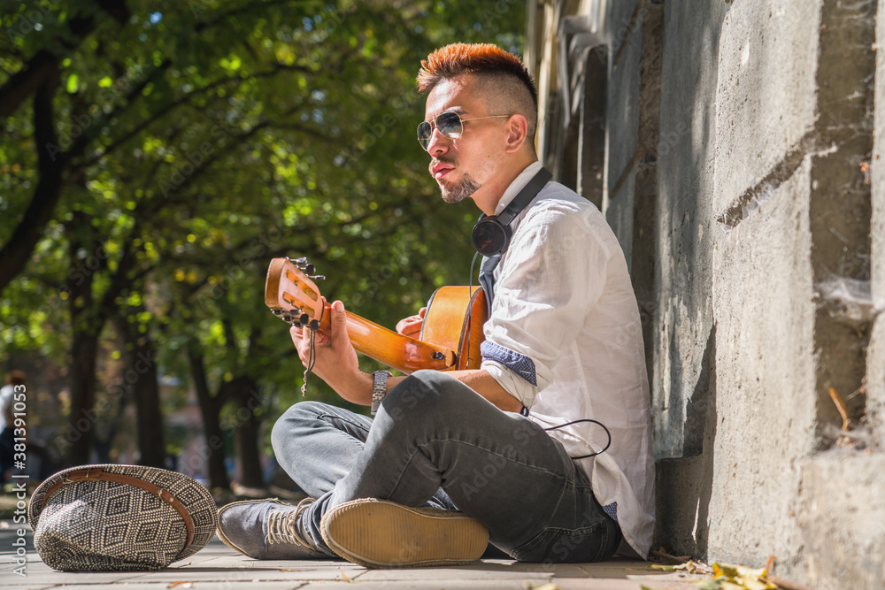Obraz premium Young male street musician playing the guitar outdoors in old european city. Horizontal image.