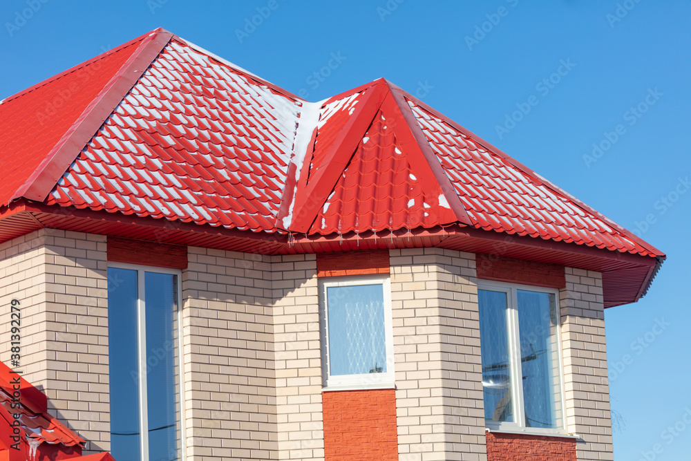 White snow lies on the red roof of the house.
