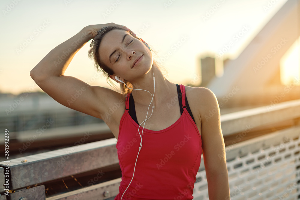 Obraz premium Female athlete stretching her neck while working out outdoors at sunset.