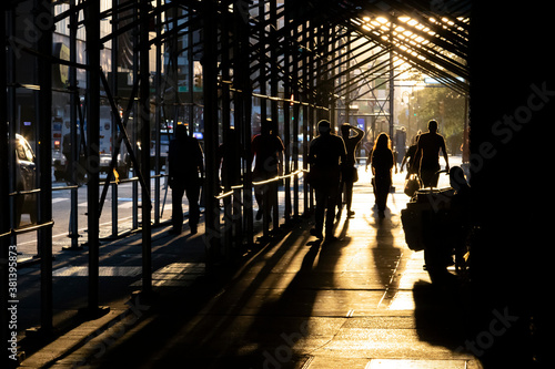 People walking down a busy sidewalk in New York City with sunlight shining through construction scaffolding overhead