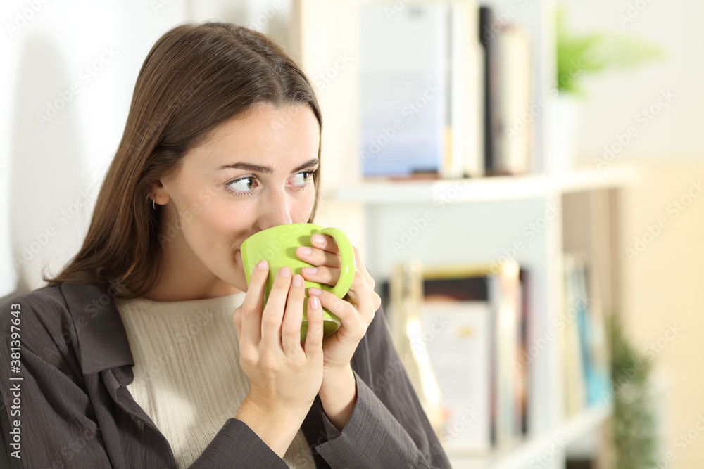 Happy woman drinking coffee looks away standing at home