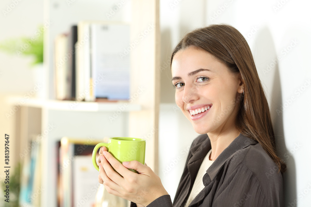 Happy woman holding coffee cup looks at camera at home Happy woman holding coffee cup looks at camera at home
