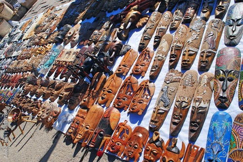 A display of traditional Egypt handcraft souvenir masks hanging from the wall on the pavement waiting for tourists. 