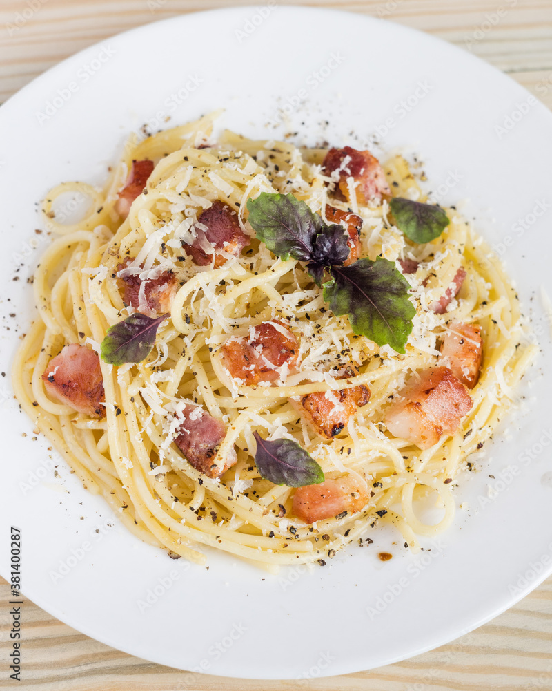 Pasta Carbonara. Spaghetti with bacon, parmesan cheese and basil on white plate on light wooden background. Italian food concept. Top view, close-up. Pasta Carbonara. Spaghetti with bacon, parmesan cheese and basil on white plate on light wooden background. Italian food concept. Top view, close-up.