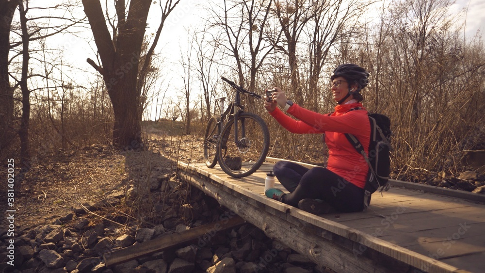 custom made wallpaper toronto digitalHappy caucasian woman cyclist makes a photo of herself a selfie on the phone while sitting on the bridge over a river in the forest in sunny weather