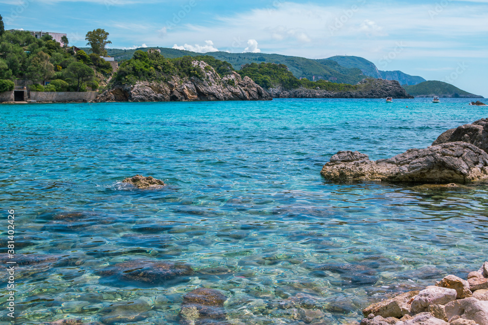 Beautiful landscape - sea lagoon with turquoise calm water, stones and rocks on the beach, blue sky. Corfu Island, Greece.