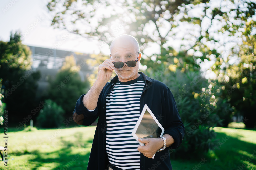 Fototapeta premium Serious stylish 50 years old male with sunglasses and tablet in city park