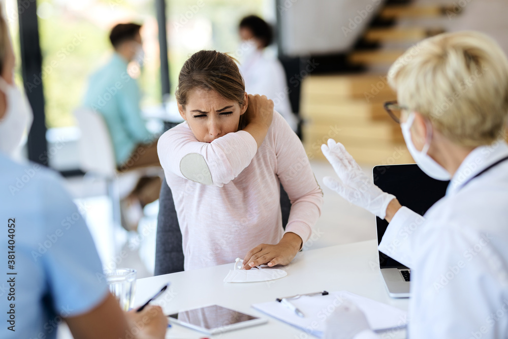 Sick woman coughing into elbow while having appointment with a doctor at the clinic. Sick woman coughing into elbow while having appointment with a doctor at the clinic.