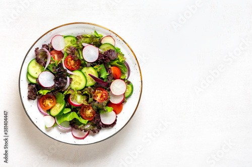 Healthy vegetable salad of cherry tomatoes, cucumber slices, green and purple lettuce leaves, onions and olive oil in plate on white wooden table Top view Flat lay Diet, mediterranean menu Vegan food
