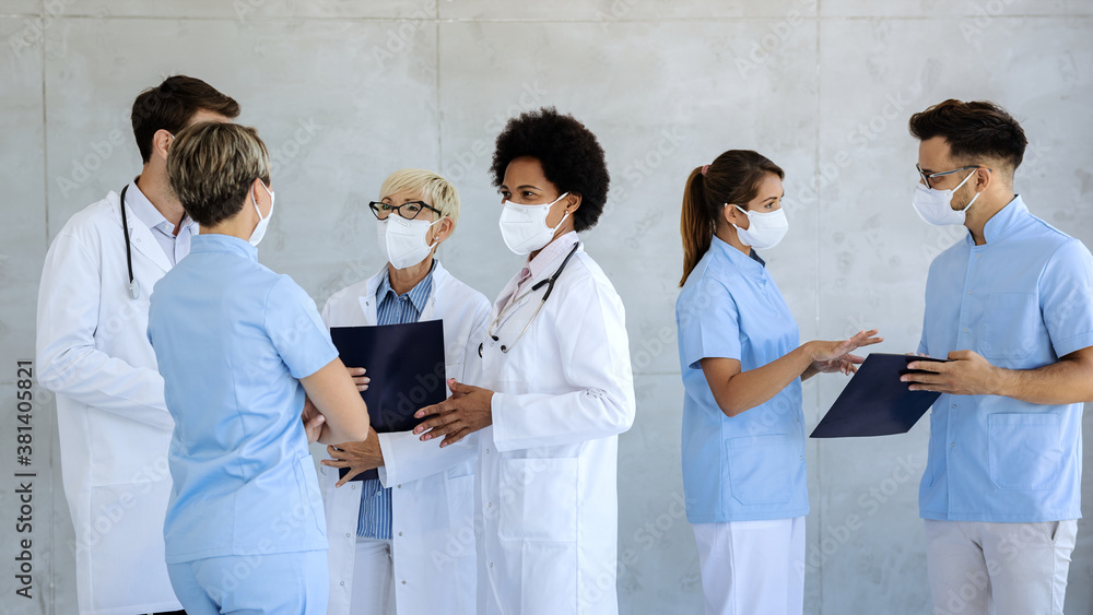 Group of healthcare workers with protective face masks talking at hospital hallway. Group of healthcare workers with protective face masks talking at hospital hallway.