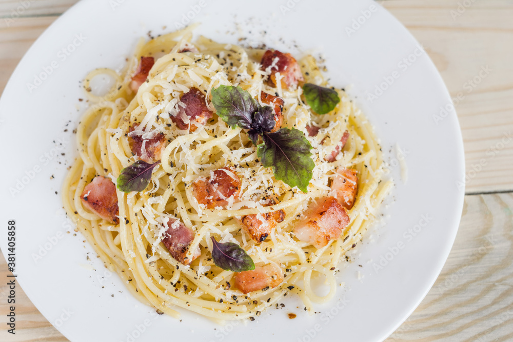 Pasta Carbonara. Spaghetti with bacon, parmesan cheese and basil on white plate on light wooden background. Italian food concept. Top view, close-up. Pasta Carbonara. Spaghetti with bacon, parmesan cheese and basil on white plate on light wooden background. Italian food concept. Top view, close-up.