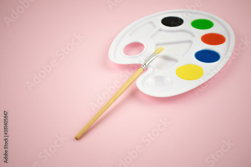 The palette of paints on a pink background with a brush. Fine art. Copyspace.