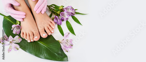 Fototapeta Naklejka Na Ścianę i Meble -  Beautiful perfect female skin legs feet top view with tropical flowers and green palm leaf. Nail polish, care and clean, spa pedicure treatment in white. Concept on background isolated. Copy space