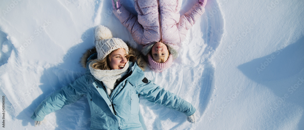 Top view portrait of cheerful mother with small daughter lying in snow in winter nature. - obrazy, fototapety, plakaty 