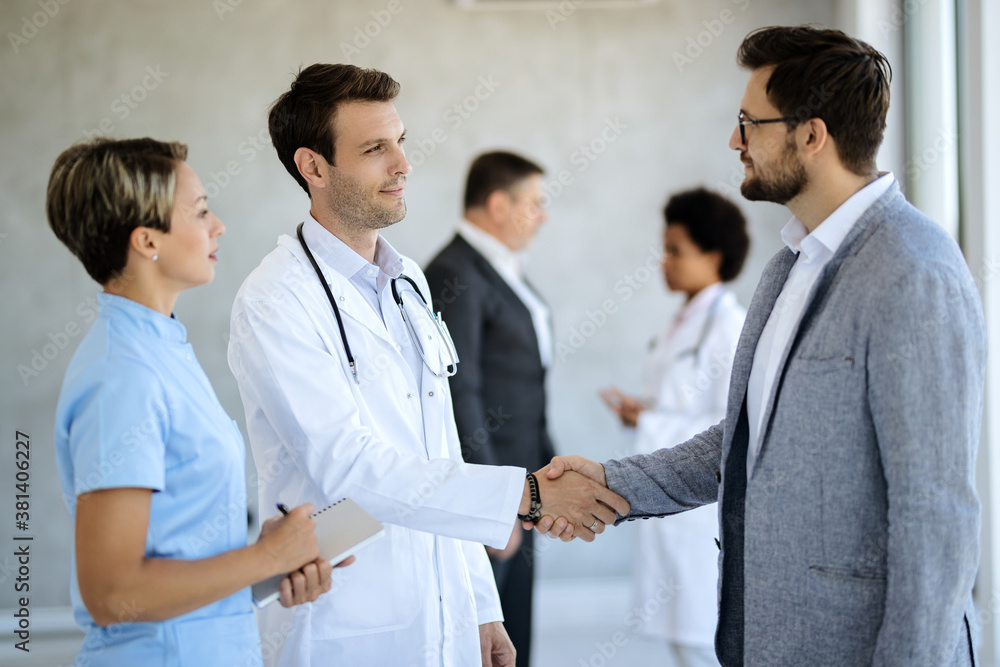 Male doctor handshaking with a businessman in hallway at the hospital. Male doctor handshaking with a businessman in hallway at the hospital.