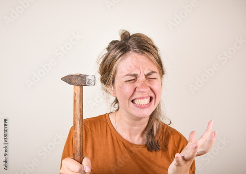 angry woman holding a hammer in her hands, unable to make repairs in the house. a woman with a hammer is angry because she cannot make repairs. Construction materials selection concept