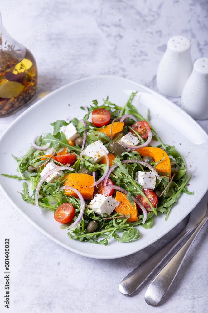 Warm salad with pumpkin, feta cheese, tomatoes, capers, arugula and red onion. Close-up. Warm salad with pumpkin, feta cheese, tomatoes, capers, arugula and red onion. Close-up.