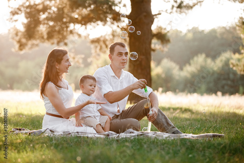 father, mother and son blow soap bubbles in the park together on a sunny summer day. happy family having fun outdoor
