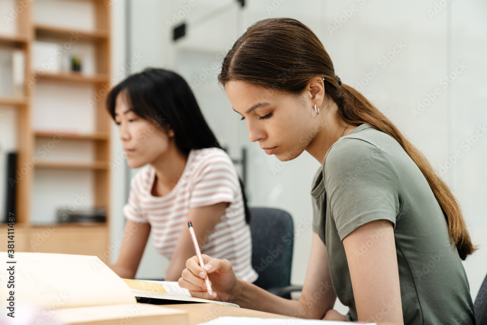 Photo of focused multinational students girls doing homework Photo of focused multinational students girls doing homework