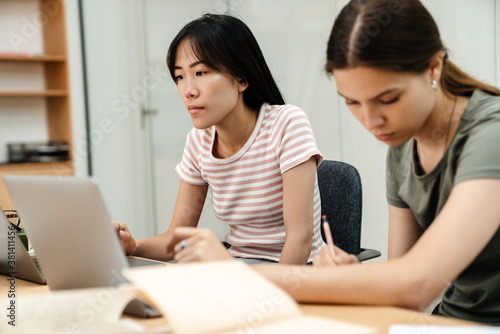 Photo of focused multinational students girls doing homework with laptops