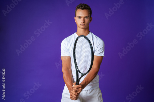 Caucasian young man tennis player posing with tennis racket against purple background © fotofabrika