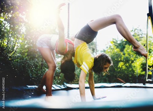 Front view of young teenager girls friends outdoors in garden, doing exercise on trampoline.
