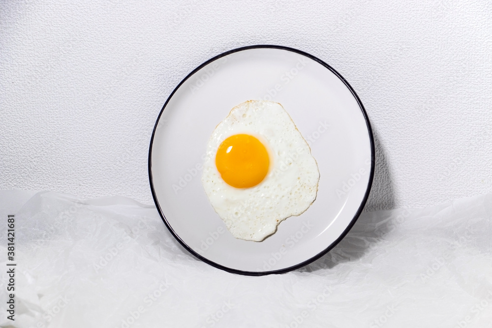 Fried egg on a white plate in a white background. Trendy food. Fried egg on a white plate in a white background. Trendy food.
