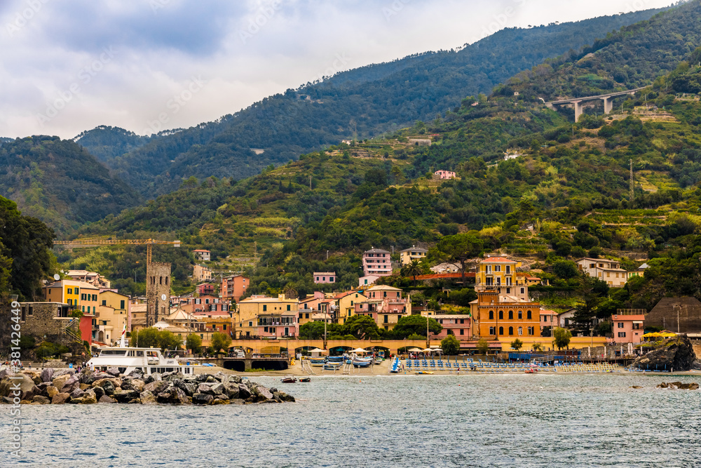 Great close-up view of the beach with the port, the medieval bell tower and the colourful buildings with the hills in the background in the old part of Monterosso al Mare; Cinque Terre coastal area.
