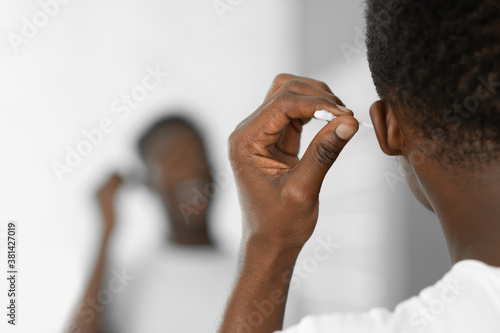 Black Man Cleaning Ears Using Cotton Swab Standing In Bathroom