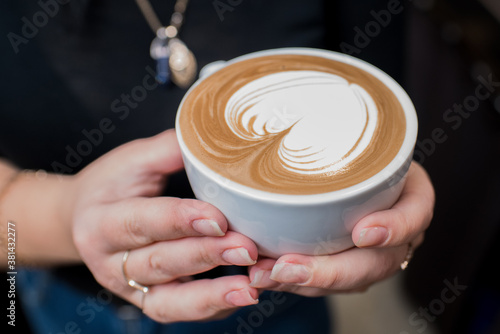 Barista girl holding fragrant freshly made cappuccino in her hands