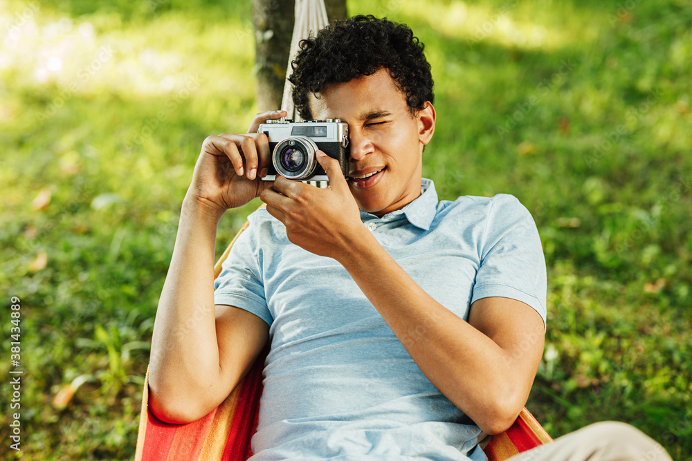 Young man making photographs on film camera while lying on a hammock in park Young man making photographs on film camera while lying on a hammock in park