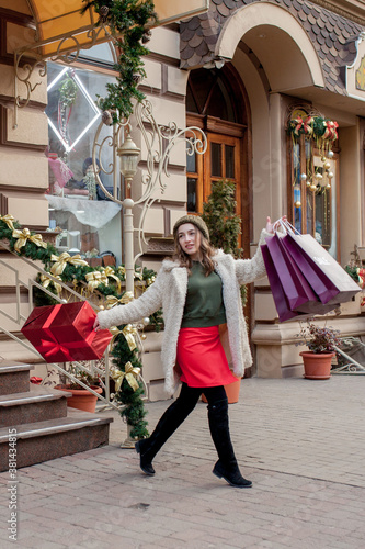 Happy woman is holding gift box in her hands and smiling leaving the store. Beautiful happy girl posing with Christmas presents. New Year preparation © volody10