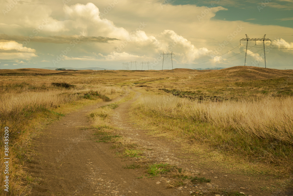 Grassland and dirt road with electric lines along, stormy skies