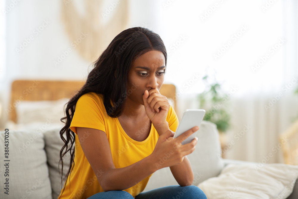 Anxious black lady reading depressing news on cellphone at home Anxious black lady reading depressing news on cellphone at home