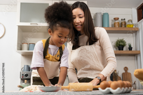 Asian woman and African little girl have fun cooking in home kitchen.