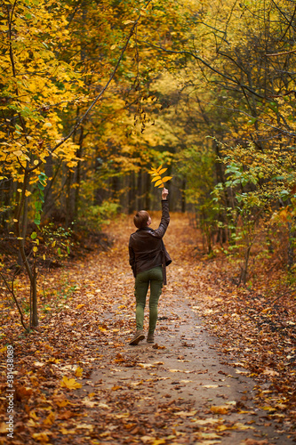 Young woman wearing brown leather jacket and green trousers walking in the autumn forest.