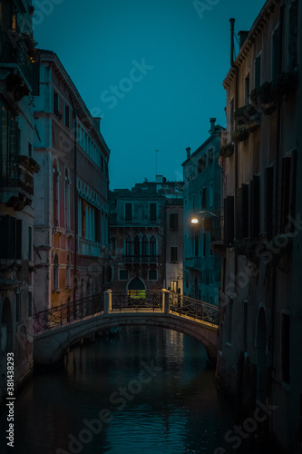 Beautiful small bridge with yellow lighting over a canal in magnificent city of Venice during night time or early evening. Blue hour in Venice, Italy.