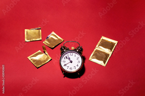 A gold watch surrounded with condoms on a red background. Special design for the contraception day. There is a space for text.
